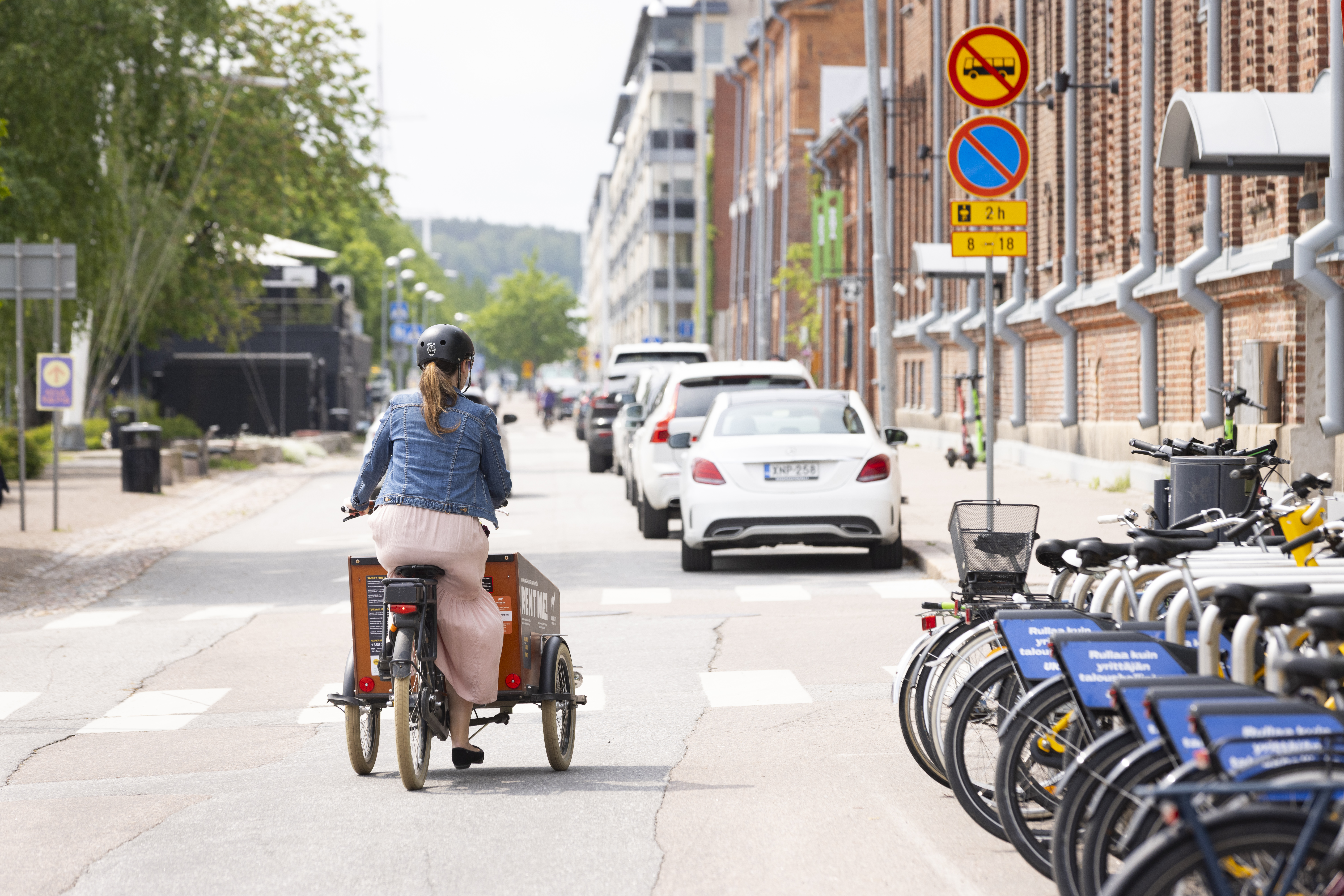 A woman is riding a cargo bike on a street her back to the camera.
