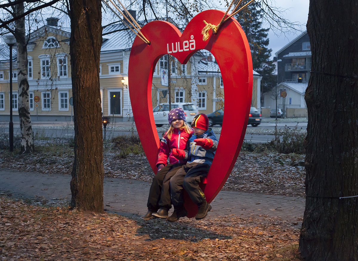 Children sitting in a heart-shaped bench with the Luleå city name written on the top
